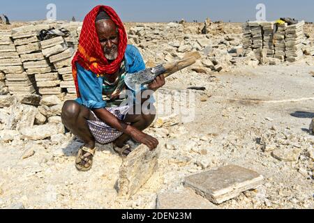 Heimischer Mann schneidet Salzböcke in einem Salzsteinbruch am Assale Salzsee, Danakil Depression, Afar Region, Äthiopien / Local man Cutting Block Stockfoto