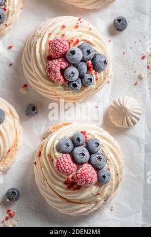 Knusprige Mini Pavlova Kuchen mit gefrorenen Früchten und Baiser auf Weißes Backpapier Stockfoto
