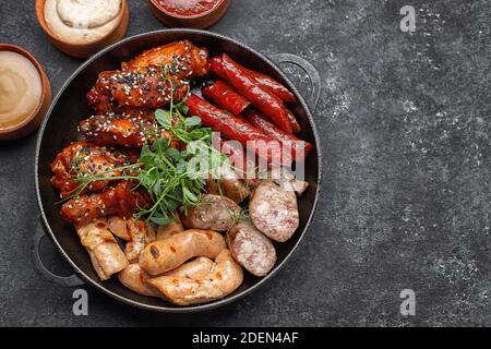 Fleischset für Bier, Wurst, Rippchen, gegrillte Flügel und drei Saucen auf schwarzem Hintergrund Stockfoto