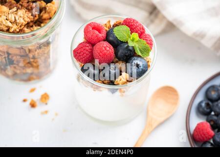 Joghurt mit Beeren und Müsli im Glas auf weißem Tisch. Sauberes Essen, Diät, gesunde Ernährung Konzept Stockfoto