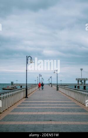 Ein Paar, das auf einer Brücke im Meer spazieren geht. Winter Herbstsaison. Stockfoto