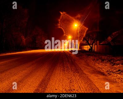 Nacht Winter verschneite Straße für Autos im Licht der Laternen. Schnee auf einer Landstraße. Straßenbeleuchtung. Winterzeit. Nachts. Nächtliche Straßenbeleuchtung. Le Stockfoto