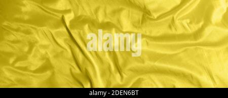 Glänzend Satin Seide Stoff mit Falten Hintergrund Textur Textil. Getönt in 2021 Farbe gelb leuchtend Stockfoto