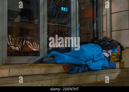 Obdachloser auf Bürgersteig schlafender Mann, Obdachloser im Winter schlafender Mann, Obdachloser im Schlafsack auf der Straße, Bürgersteig, Berlin unter den Linden Stockfoto