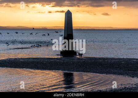 Southend on Sea, Essex, Großbritannien. Dezember 2020. Der erste Tag im Dezember ist zu Ende, als er begann; hell, aber sehr kalt. Die Sonne unterging hinter einer Wolkenschicht hinter dem Crowstone im Stadtteil Chalkwell von Southend. Der Crowstone ist ein historischer Markerstein, auch bekannt als London Stone, in der Themse Mündung, die früher die Grenzen der Gerichtsbarkeit der City of London markiert und stammt aus dem Jahr 1837. Steine standen auf dem Gelände aus den 1200er Jahren. Seevögel Stockfoto