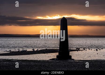 Southend on Sea, Essex, Großbritannien. Dezember 2020. Der erste Tag im Dezember ist zu Ende, als er begann; hell, aber sehr kalt. Die Sonne unterging hinter einer Wolkenschicht hinter dem Crowstone im Stadtteil Chalkwell von Southend. Der Crowstone ist ein historischer Markerstein, auch bekannt als London Stone, in der Themse Mündung, die früher die Grenzen der Gerichtsbarkeit der City of London markiert und stammt aus dem Jahr 1837. Steine standen auf dem Gelände aus den 1200er Jahren. Seevögel Stockfoto