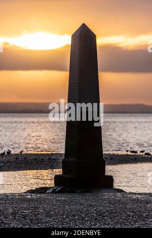 Southend on Sea, Essex, Großbritannien. Dezember 2020. Der erste Tag im Dezember ist zu Ende, als er begann; hell, aber sehr kalt. Die Sonne unterging hinter einer Wolkenschicht hinter dem Crowstone im Stadtteil Chalkwell von Southend. Der Crowstone ist ein historischer Markerstein, auch bekannt als London Stone, in der Themse Mündung, die früher die Grenzen der Gerichtsbarkeit der City of London markiert und stammt aus dem Jahr 1837. Steine standen auf dem Gelände aus den 1200er Jahren. Seevögel Stockfoto