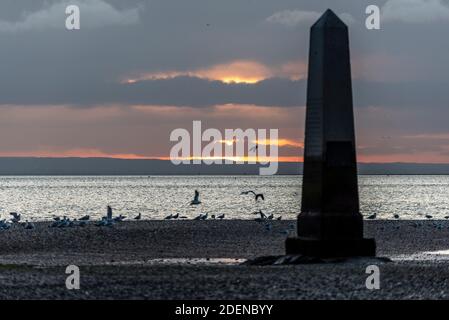 Southend on Sea, Essex, Großbritannien. Dezember 2020. Der erste Tag im Dezember ist zu Ende, als er begann; hell, aber sehr kalt. Die Sonne unterging hinter einer Wolkenschicht hinter dem Crowstone im Stadtteil Chalkwell von Southend. Der Crowstone ist ein historischer Markerstein, auch bekannt als London Stone, in der Themse Mündung, die früher die Grenzen der Gerichtsbarkeit der City of London markiert und stammt aus dem Jahr 1837. Steine standen auf dem Gelände aus den 1200er Jahren. Seevögel Stockfoto