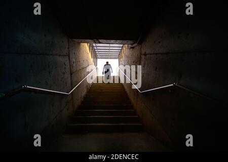 Mann, der von der Leiter zum Licht in der dunklen Umgebung geht. Stockfoto