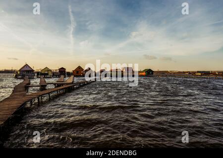 Dorf über dem See Bokod in den frühen Sonnenuntergang gefangen gebaut. Hölzerne Gehwege, die zu kleinen Fischerhäusern führen, die auf dem Wasser schwimmen. Ungarn, Europa Stockfoto