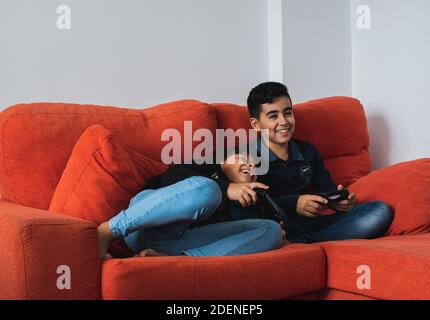 Ein sehr glückliches und lächelndes Mädchen und Jungen, die zu Hause auf dem Sofa sitzen und Videospiele spielen. Stockfoto