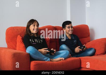 Ein sehr glückliches und lächelndes Mädchen und Jungen, die zu Hause auf dem Sofa sitzen und Videospiele spielen. Stockfoto
