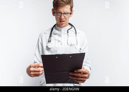 Ein nachdenklicher Arzt, der die Dokumente betrachtet und Notizen in den Dokumenten macht, ein junger Student mit einem Ordner in den Händen, auf weißem Hintergrund, Stockfoto