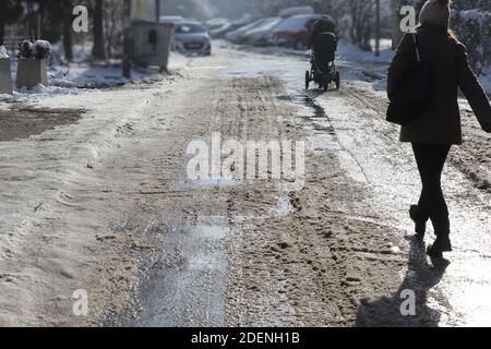 Die Leute laufen auf einer unbeputzten, vereisten Straße. Rutschige Straße im Winter. Stockfoto