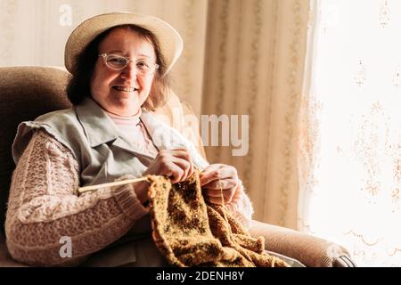 Ältere Frau strickt Pullover für ihre Enkel am Fenster Stockfoto