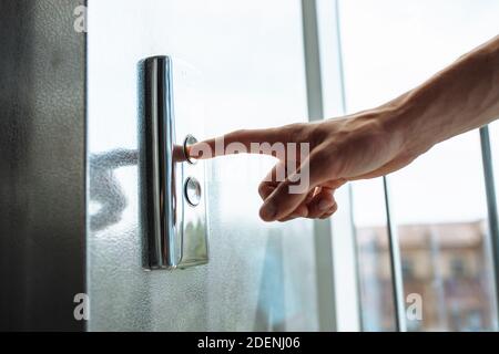 Der Daumen drückt die Elevator-Taste, eine Hand, die nach der Taste greift, das Mädchen wartet auf Elevator, Drucktaste Start, isoliert Stockfoto