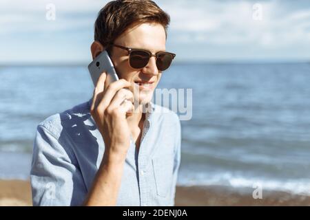 Schöne stilvolle Business-Kerl mit Brille, posiert am Strand, Hipster am Telefon sprechen, Arbeit im Urlaub, Stockfoto