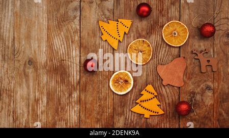 Trockene Orangen, rote Kugeln und Weihnachtsfiguren aus Holz auf rustikalem braunen Holzhintergrund mit Platz für Text Stockfoto