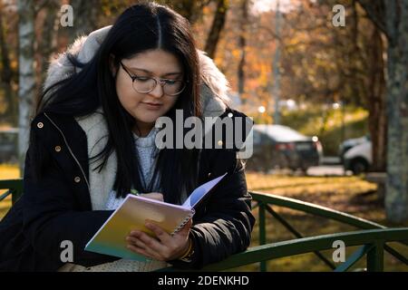 Frau, die im Park liest. Frau, die sich Notizen im Notizbuch gemacht hat. Stockfoto