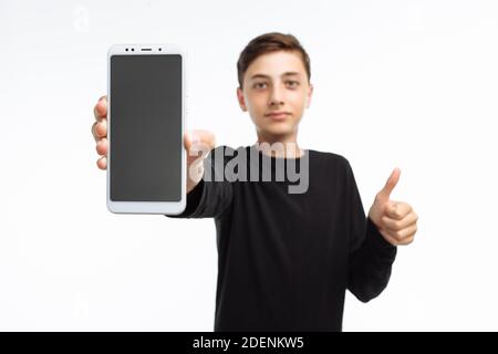 Porträt eines Teenagers, eines Mannes, der ein Telefon mit einem weißen Bildschirm hält, und zeigt eine Fingerklasse, in einem schwarzen T-Shirt, auf weißem Hintergrund, Stockfoto