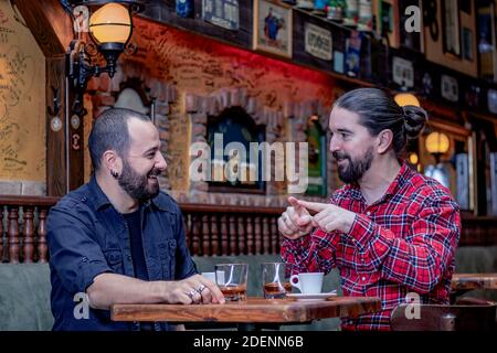 Zwei männliche Freunde trinken gemeinsam Whiskey und Kaffee im Pub. Beste Freunde reden, gestikulieren und eine gute Zeit haben. Stockfoto