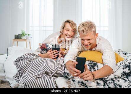 Teens Pärchen liegt in einem gemütlichen Bett im Schlafzimmer und surfen gemeinsam im Internet oder checken Mails mit einem modernen Smartphone. Moderne Technologie oder Coup Stockfoto