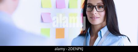 Geschäftsfrau in Brille steht neben Whiteboard gegenüber Kollegen. Stockfoto