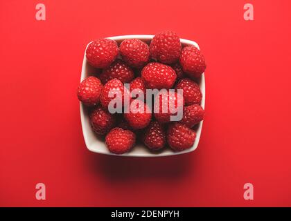 Nahaufnahme von Himbeeren in einer Schüssel auf rotem Hintergrund.Selektiver Fokus Stockfoto