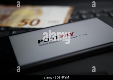 Viersen, Deutschland - 9. April. 2020: Nahaufnahme des Handybildschirms mit Logo-Schriftzug des Postpay Payment Providers auf Computertastatur, verschwommene Euro m Stockfoto