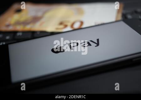 Viersen, Deutschland - 9. April. 2020: Nahaufnahme des Handybildschirms mit Logo-Schriftzug des Apple Pay Payment Providers auf Computertastatur, verschwommener Euro Stockfoto