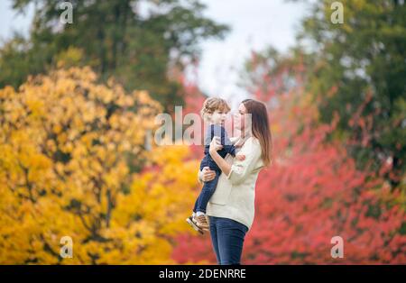 Eine junge Mutter und ihr Sohn spielen in der park gegen schöne Herbstfarben veranschaulichen das Glück und die Freude Der Familie Stockfoto