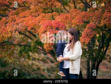 Mutter und Sohn knurren gegen den bunten Herbstbaum Stockfoto