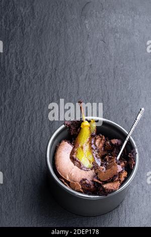 Schokoladenkuchen-Brownie mit pochierter Birne im Tontopf Schwarzer Stein Hintergrund Stockfoto