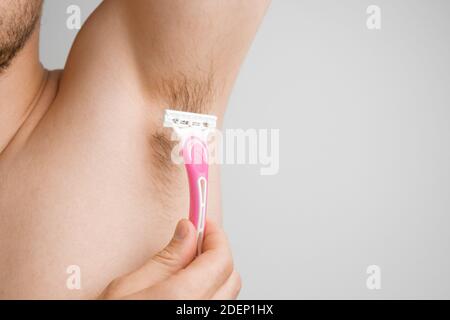 Nahaufnahme Mann rasiert haarige Achselhöhlen mit einem rosa Rasiermesser. Unrasierte Achselhöhlen oder Achselhöhlen. Enthaarung und Haarentfernung Verfahren Stockfoto