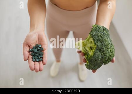 Frau hält frischen Brokkoli Kopf und Spirulina Pillen vor der Herstellung Gesunder Smoothie Stockfoto