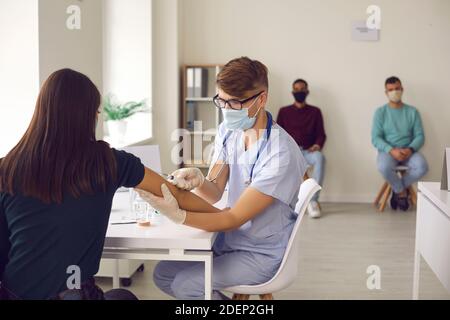 Junger Arzt in einer medizinischen Gesichtsmaske, die eine Grippe gibt Oder Covid-19-Impfstoff an eine asiatische Frau Stockfoto