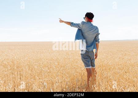 Ein Mann zeigt in die Ferne auf einem Weizenfeld, ein Tourist im Urlaub Stockfoto