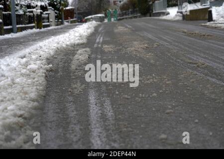 Die Straße ist durch den Verkehr mit einem nassen, schmutzigen Schnee bedeckt. Auf der linken Seite gibt es einen Seitenweg. Zwischen Straße und Seitenweg liegt eine Schneeschicht. Stockfoto