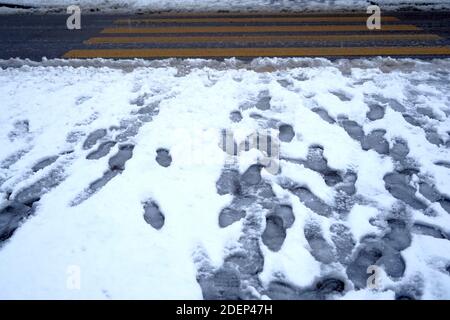 Schuhabdrücke und Hundepfoten im schneebedeckten Gehweg. Der Schnee wurde nicht weggewischt. Fußgängerübergänge im Hintergrund werden gelöscht. Stockfoto