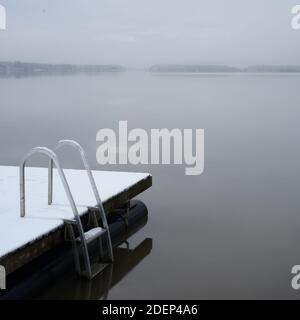Holzsteg und Leiter auf dem mit Schnee bedeckten See Stockfoto
