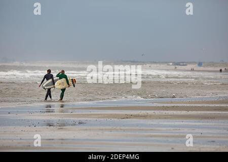 Surfer, die bei kaltem Wind ins Wasser kommen Stockfoto