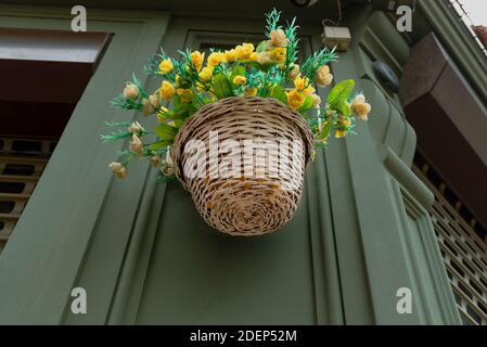 Ein Korb mit gelben künstlichen Blumen hängt an der Ecke eines Gebäudes. Stockfoto