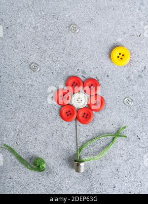 Nähthema kreatives Flat Lay-Design: Blume in einem Blumentopf unter der Sonne aus Nadel, Faden, Handballen und Knöpfen auf grauer Oberfläche Stockfoto