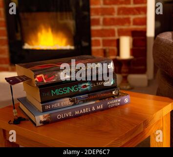 Ein Stapel Bücher auf einem Couchtisch vor einem echten elektrischen Feuer mit Flammeneffekt. Stockfoto