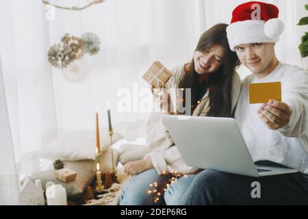Glücklicher Ehemann mit Kreditkarte und Kauf von Geschenken für Frau oder Familie, Online-Shopping am Black Friday mit Laptop in einem modernen Zimmer mit festlichem Holid Stockfoto