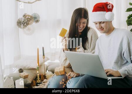 Weihnachtsverkäufe und Online-Home-Shopping. Happy stylish Familie Online-Shopping am Black Friday mit Laptop und Kreditkarte, sitzen in modernen Zimmer w Stockfoto