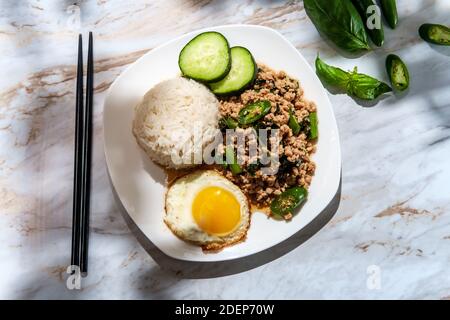 Phat Krapow Mu SAP auch bekannt als Rührgebratenes Thai-Basilikum Schweinefleisch mit Austernsauce serviert mit weißem Reis und ein Spiegelei sunnyside oben Stockfoto