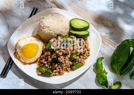 Phat Krapow Mu SAP auch bekannt als Rührgebratenes Thai-Basilikum Schweinefleisch mit Austernsauce serviert mit weißem Reis und ein Spiegelei sunnyside oben Stockfoto