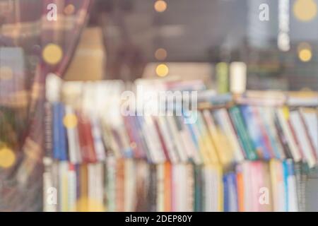 Verschwommene Bücherregale mit bunten Büchern, die hinter dem Schaufenster liegen. Bücher lesen und verkaufen. Für den Hintergrund Stockfoto