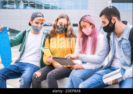 Multirassische Teenager-Freunde tragen Gesichtsmaske sitzen auf tha Bank Außerhalb der Schule - Neue normale Lifestyle-Konzept mit jungen Studenten, die sich zusammenstocken Stockfoto